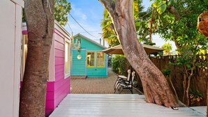 A colorful house with a pink and teal exterior, a wooden deck, and a chair under a tree.