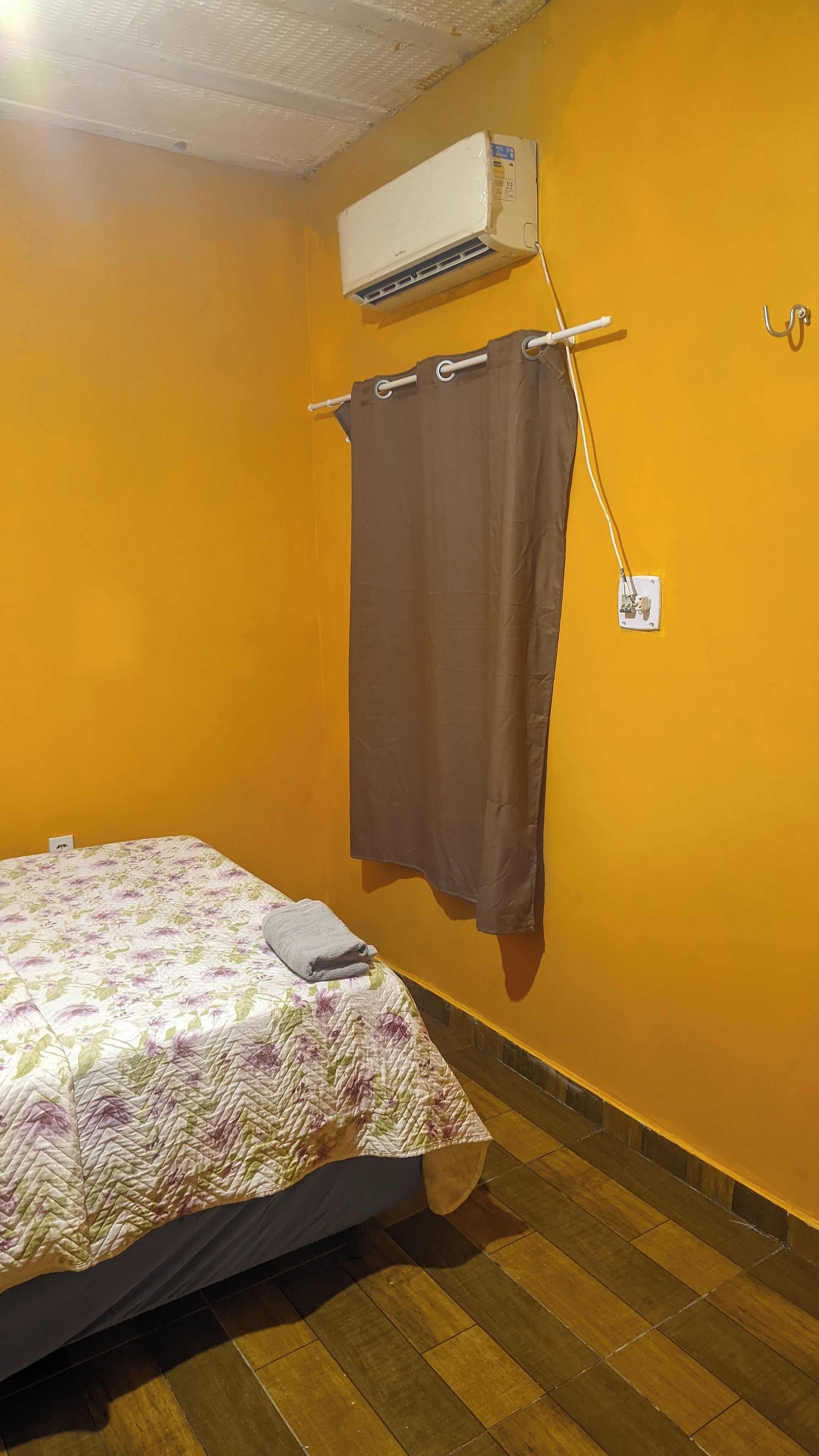 A room with a bed, an air conditioning unit, a curtain, and a wall-mounted hook.