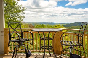 A deck with two metal chairs and a small round table, overlooking a scenic landscape with trees and hills. - Charming Mountain Home with a View (Seven Devils)