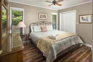 A bedroom with a bed, bedside table, lamp, and a view of greenery outside. - Charming Mountain Home with a View (Seven Devils)