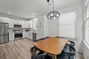Een moderne keuken met witte kasten, roestvrijstalen apparatuur en een houten eettafel met zwarte stoelen.