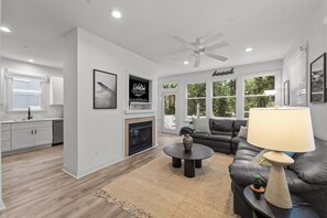 A modern living room with a fireplace, a sofa, a coffee table, and a ceiling fan. - Walk on Water: Soundside, Community Pool and Clubhouse Access (Kill Devil Hills)