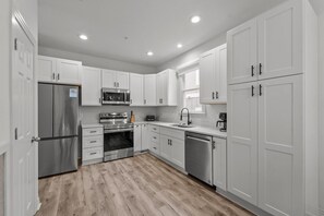 A modern kitchen with white cabinets, stainless steel appliances, and a wooden floor. - Walk on Water: Soundside, Community Pool and Clubhouse Access (Kill Devil Hills)