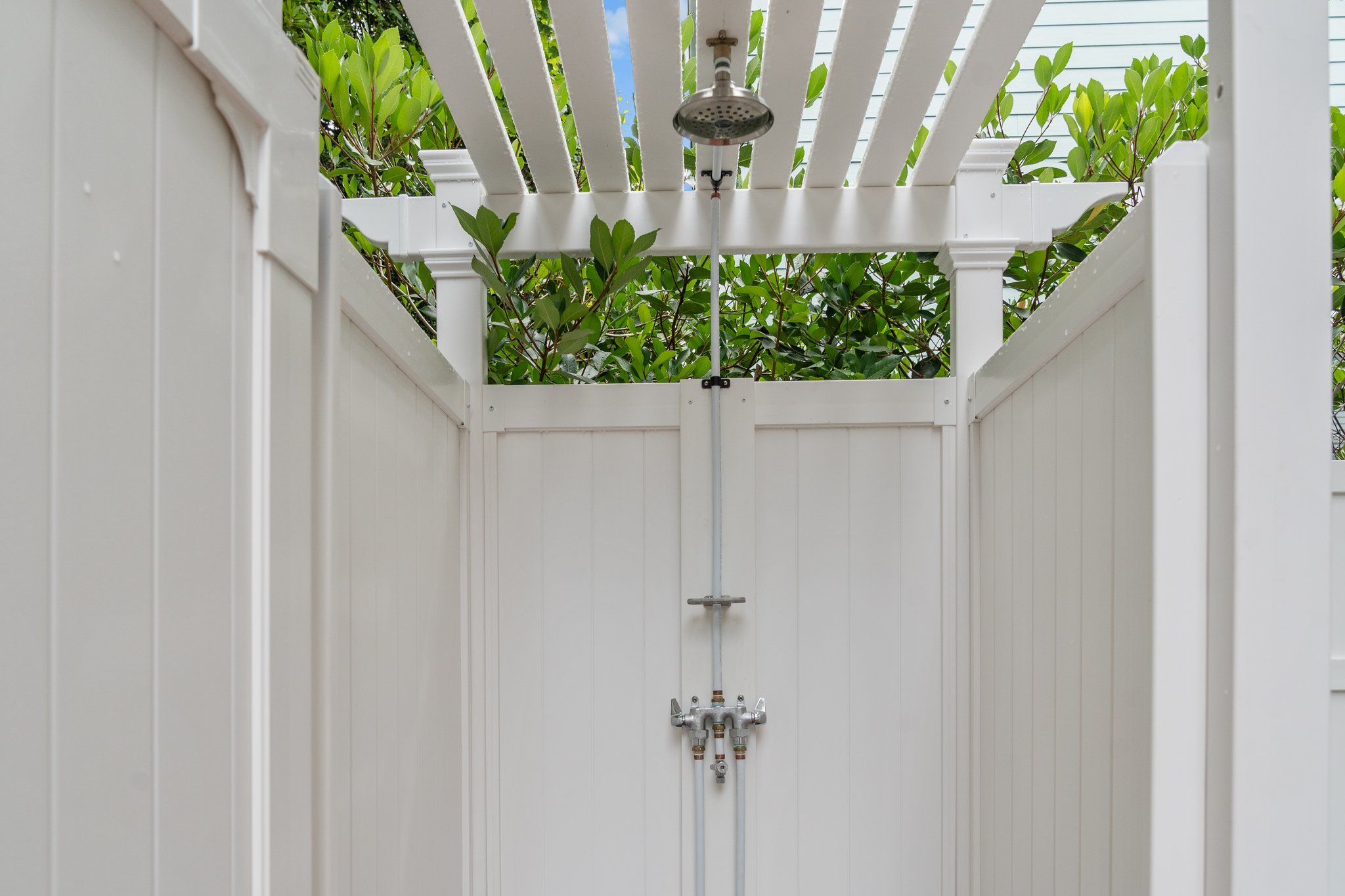 A white wooden pergola with a showerhead and pipes.