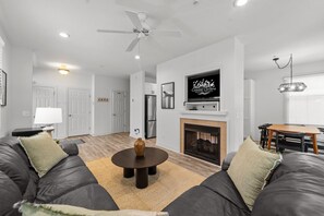 A modern living room with a fireplace, a ceiling fan, and a television mounted above it.