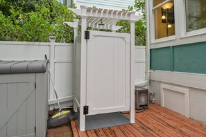 Valkoinen puinen portti, jonka yläpuolella on pergola, porttiin nojaava harja ja puinen terassi.