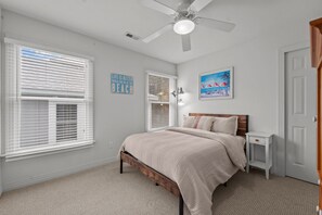 A bedroom with a bed, two windows with blinds, a ceiling fan, a nightstand, and a door.
