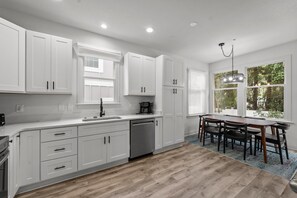 A modern kitchen with white cabinetry, a dishwasher, a coffee maker, and a dining area with a table and chairs.