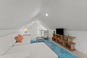 A modern loft bedroom with a large bed, a sofa, a coffee table, a TV, and a wooden shelf.
