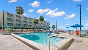 A swimming pool with a clear blue water, surrounded by lounge chairs and umbrellas, with a building in the background. - Beautiful Two Bedroom, Two Bath Condo at Sailport (Tampa)