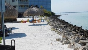 A beach with thatched umbrellas, colorful lounge chairs, and a rocky shoreline. - Beautiful Two Bedroom, Two Bath Condo at Sailport (Tampa)