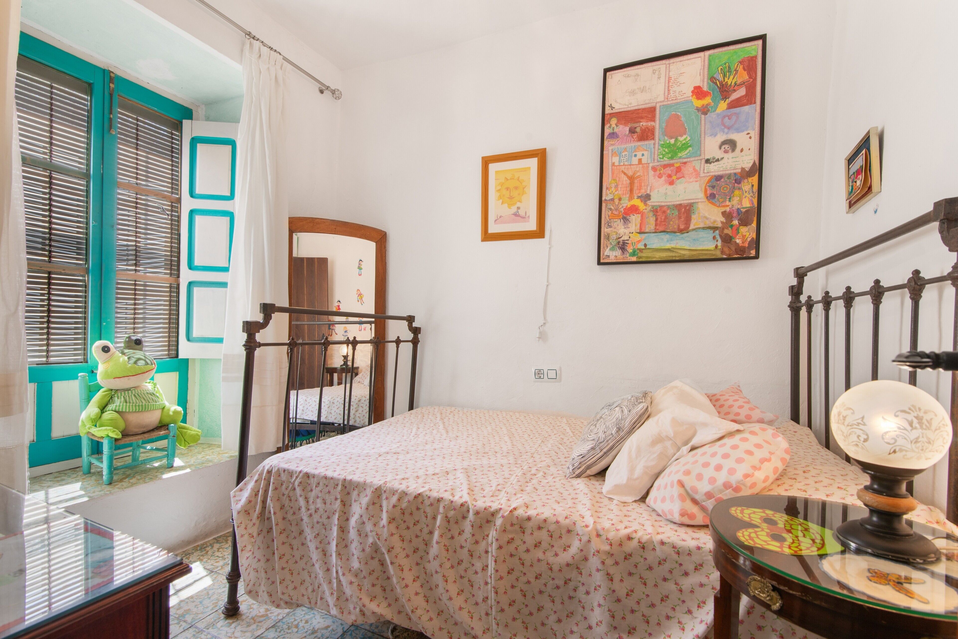 Un dormitorio con cama, cómoda, espejo, ventana con cortinas y una decoración con sapo.