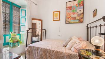 Un dormitorio con cama, cómoda, espejo, ventana con cortinas y una decoración con sapo.