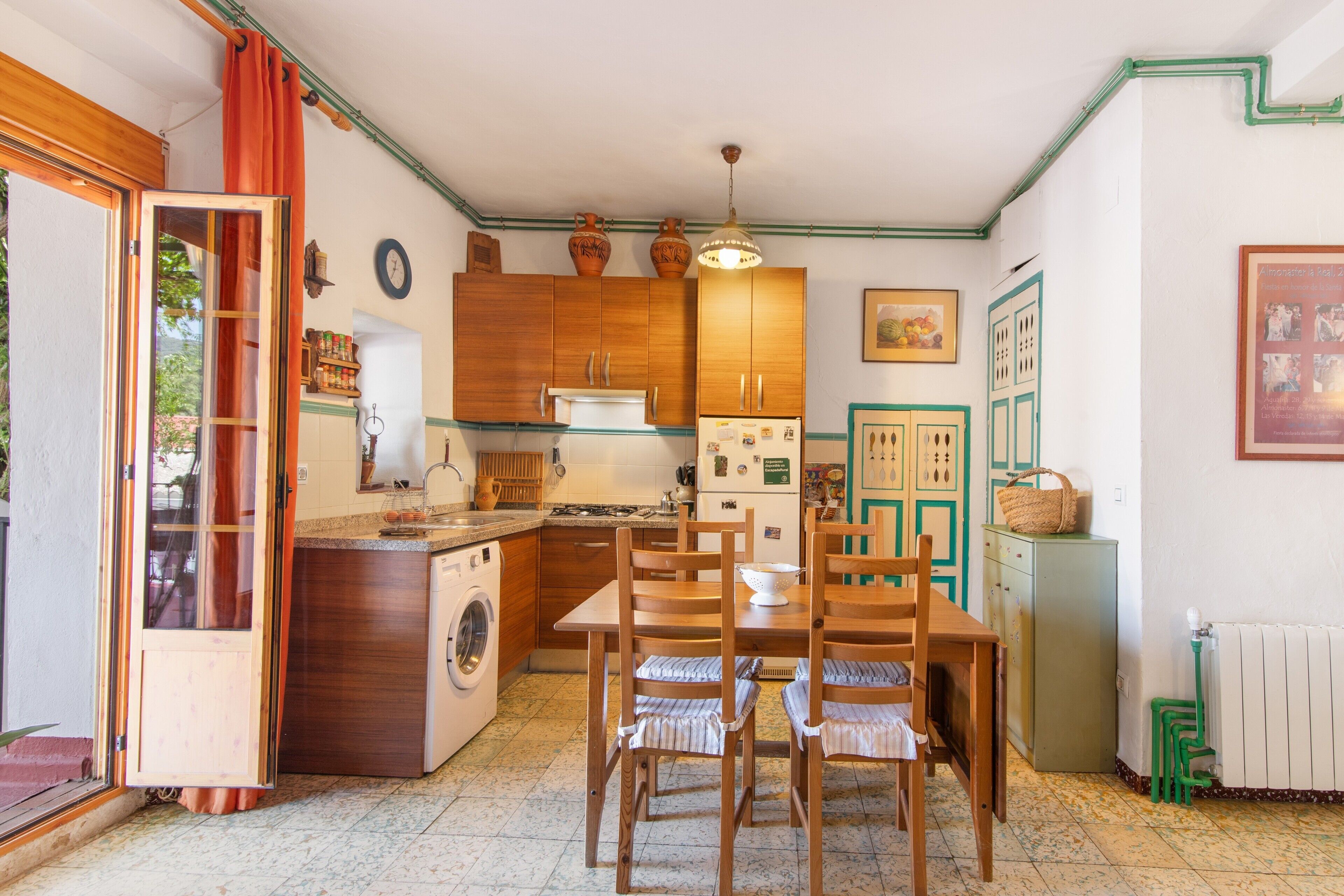 Una cocina compacta con armarios de madera, una mesa de comedor con sillas, una lavadora y un refrigerador pequeño.