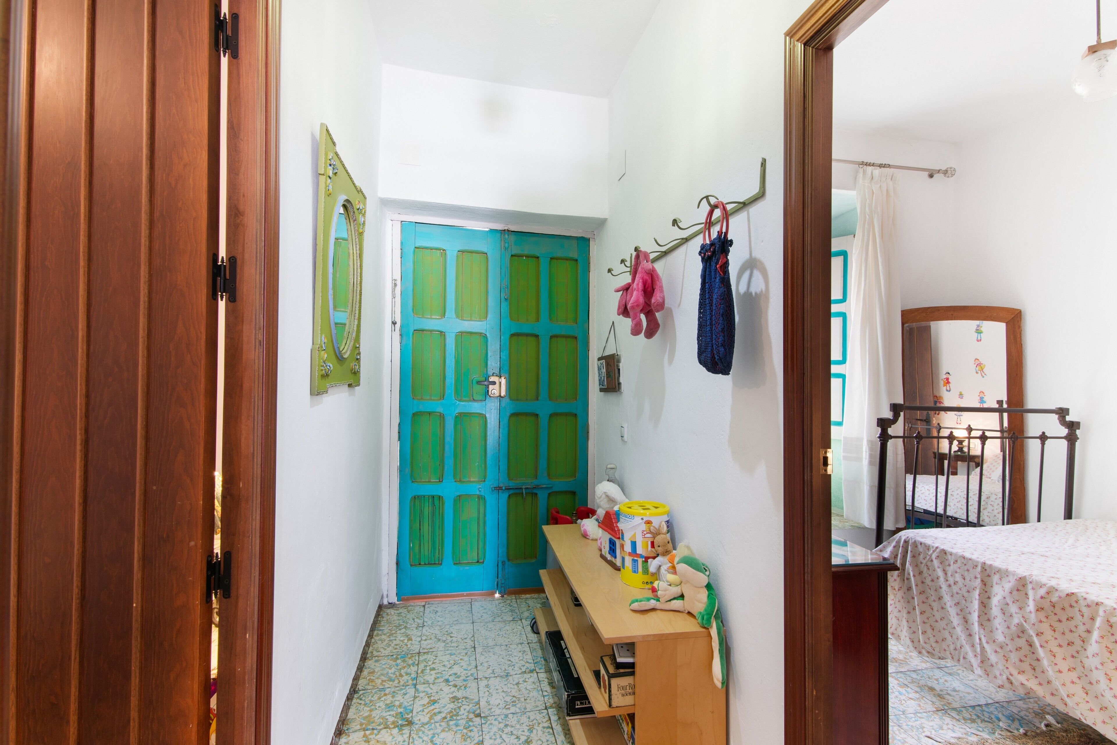 Una habitación con puerta de madera, puerta azul, cama, escritorio con objetos y espejo.