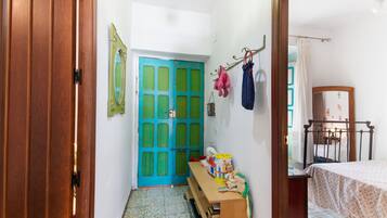 Una habitación con puerta de madera, puerta azul, cama, escritorio con objetos y espejo.