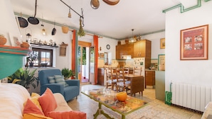 A cozy living room with a sofa, chairs, a coffee table, and a kitchen area with wooden cabinets and a dining table. - Country House 'La Rana Verde De Arriba' with Mountain Views, Private Terrace & Wi-Fi (Los Romeros)