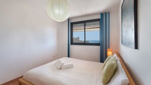 Een slaapkamer met een bed, een hanglamp, een raam met zonwering, en een kunstwerk aan de muur.