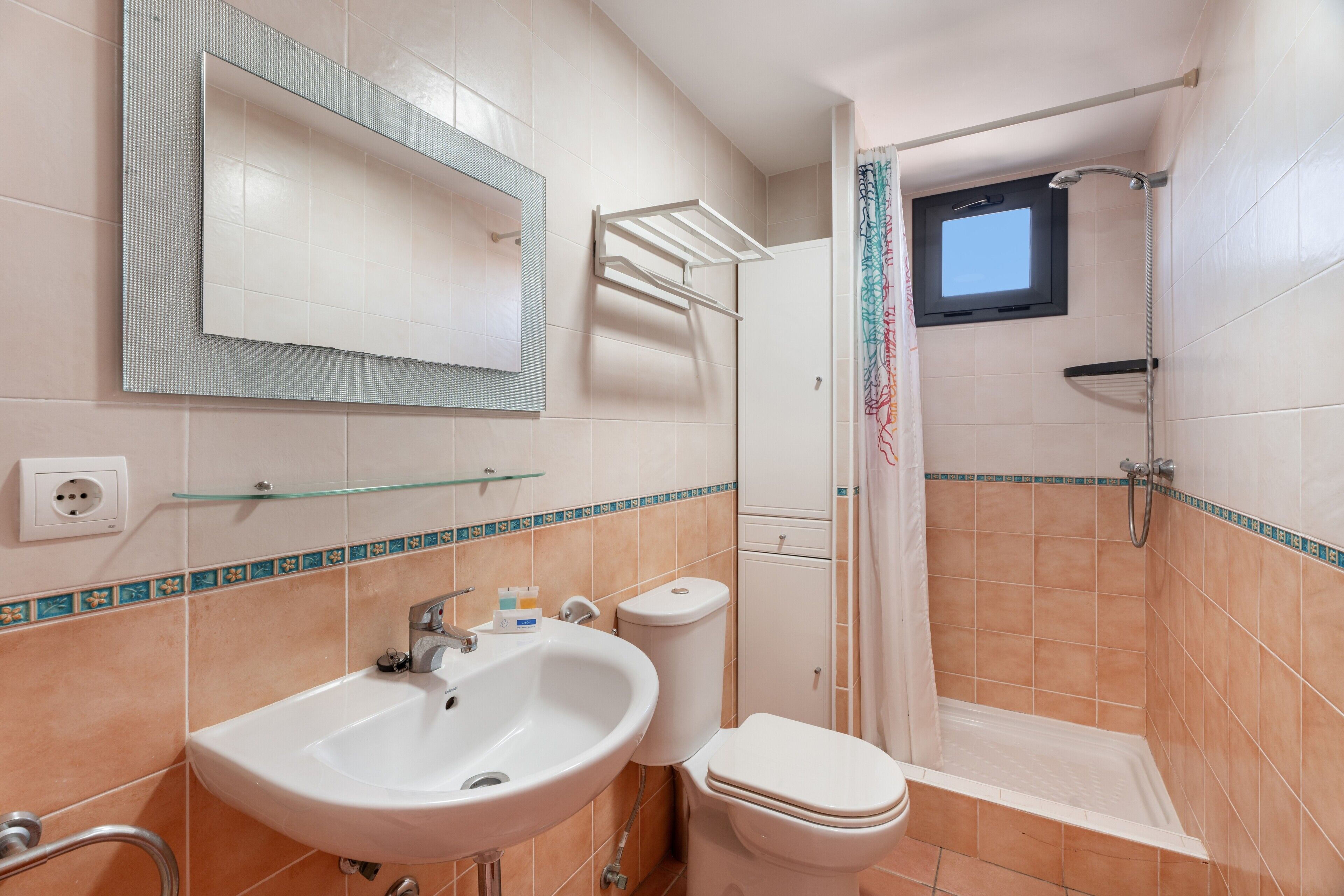 A bathroom with a sink, toilet, shower, and a small window.