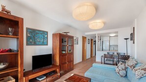 Een woonkamer met een televisie, houten meubels, een bank en een eethoek met stoelen en een tafel.