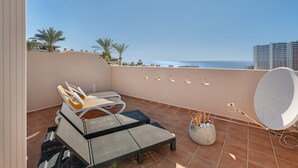Een balkon met uitzicht op zee, een schotelantenne en een zithoek met kussens.