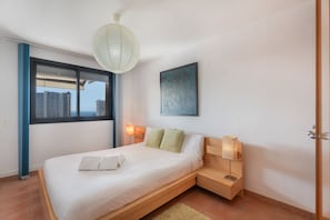A modern bedroom with a bed, bedside lamps, a view through a window, and a painting on the wall.