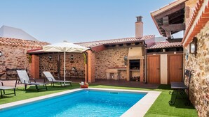 Una piscina con sillas de descanso, un porche cubierto, muros de piedra y una chimenea de ladrillo.