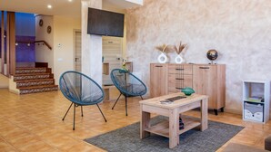 Una sala de estar moderna con una mesa de centro de madera, dos sillas azules, un aparador con objetos decorativos y una escalera al fondo.