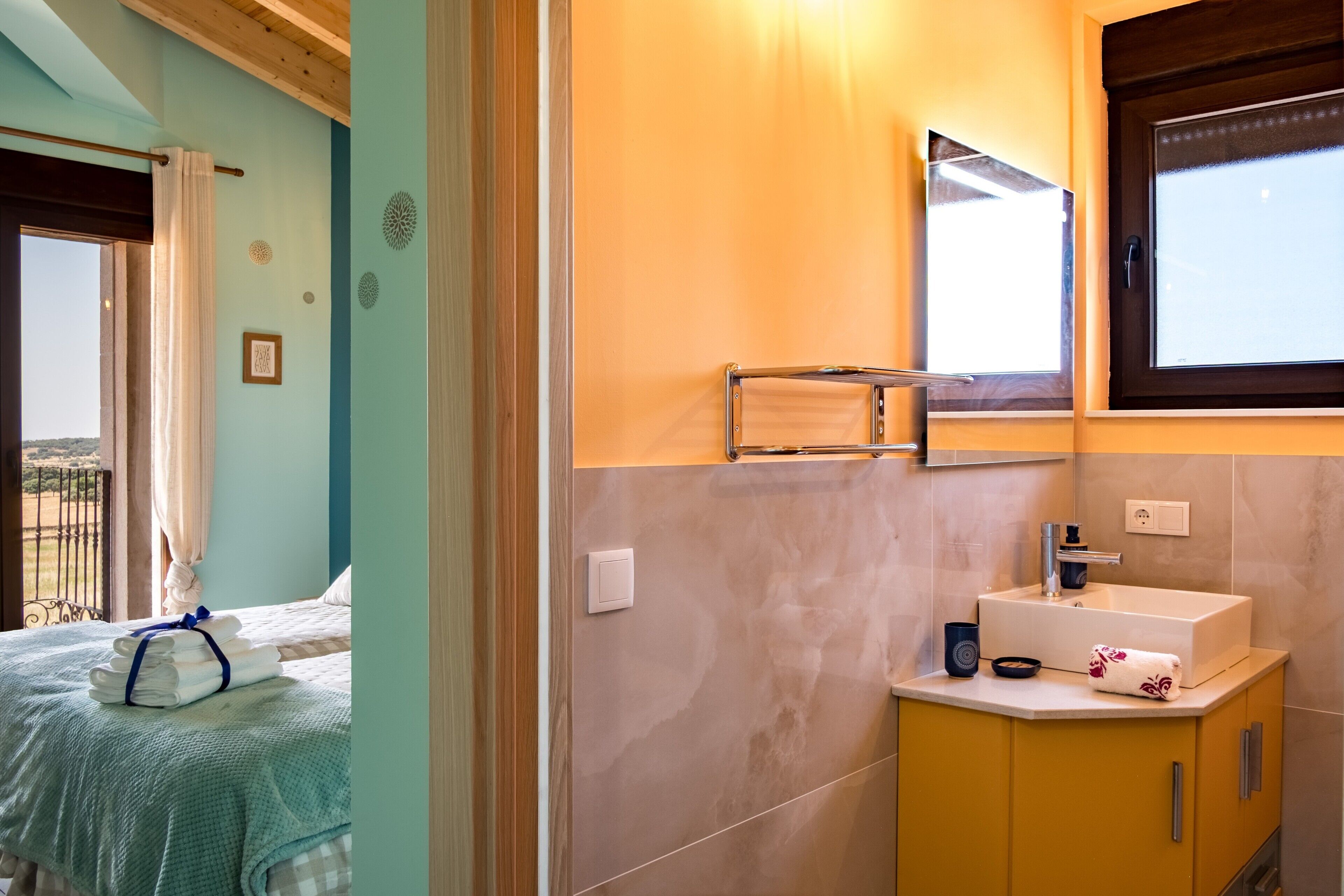 Un dormitorio con cama, un baño con lavamanos y espejo, y vistas al exterior.