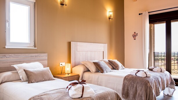 Habitación de hotel con dos camas, una mesita de noche, una lámpara y vistas al exterior.