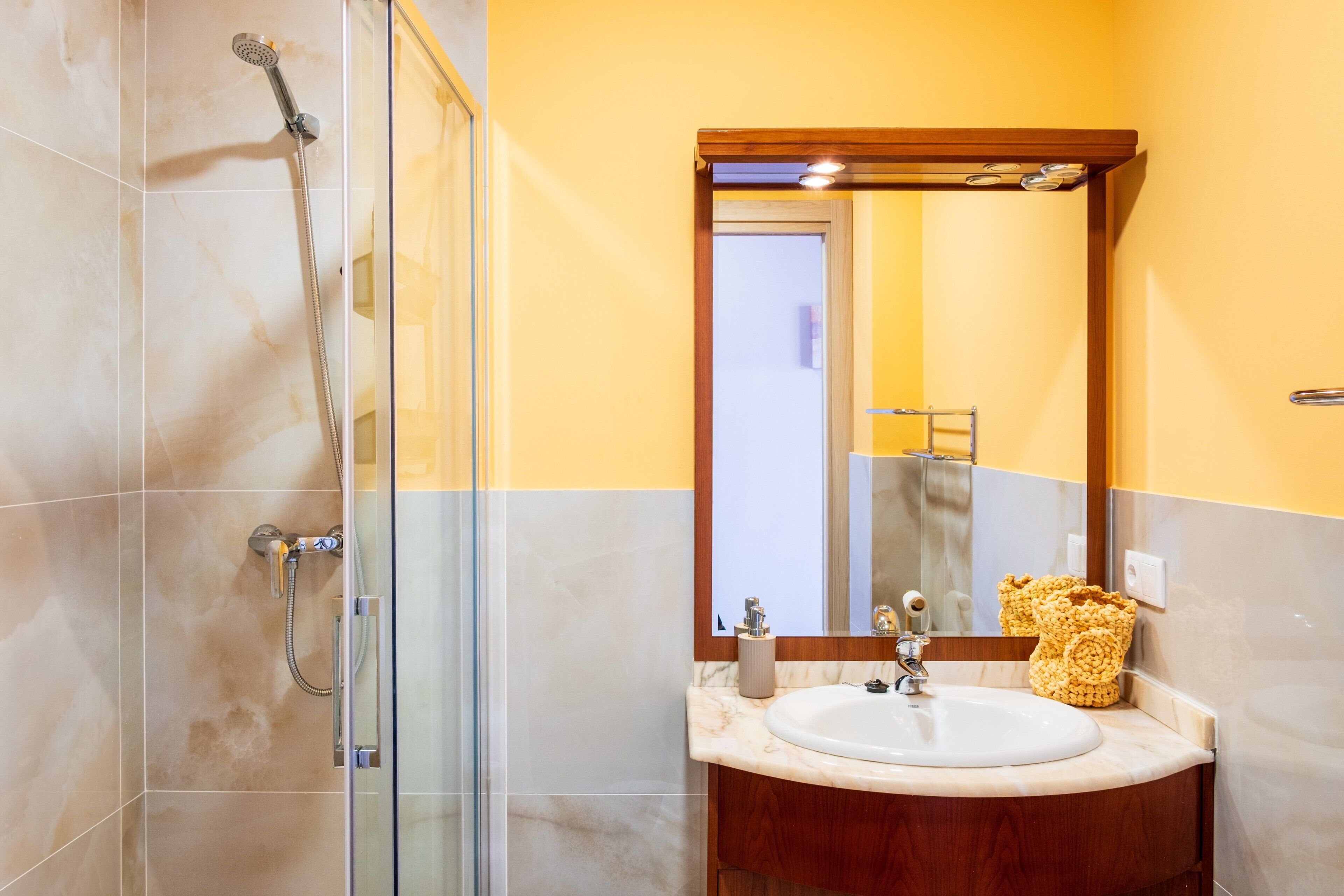 Un baño con ducha de vidrio, un lavamanos con tocador de madera y un espejo sobre el lavamanos.