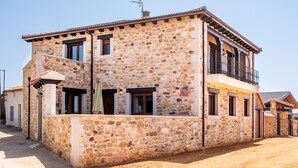 Un edificio de piedra de dos pisos con un balcón, un porche pequeño y un camino de tierra.