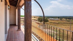 Un balcón con vistas a un paisaje rural, que incluye campos y edificios lejanos.