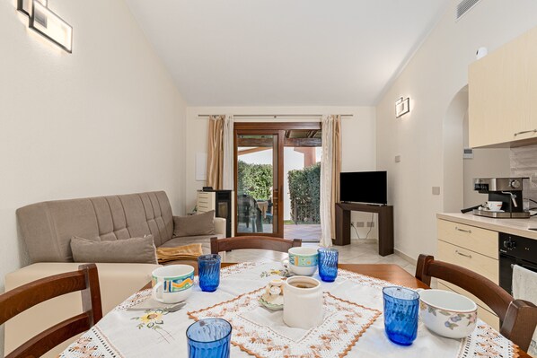 A dining area with a table set for two, a sofa, and a kitchen in the background.