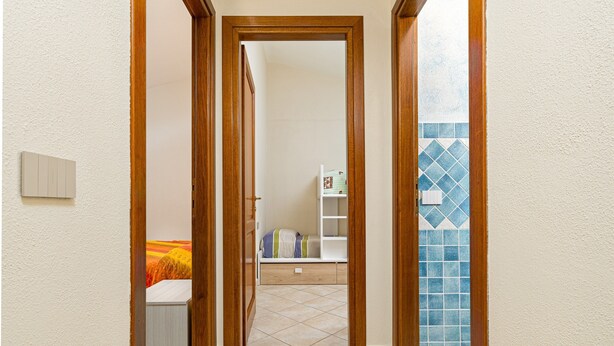Ein Korridor mit Holztüren, die zu einem Zimmer mit einem Bett und einem Regal führen.