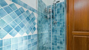 Ein Badezimmer mit blauen Mosaikfliesen, einer Duschkabine und einer Holztür.
