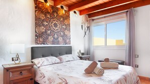 Un dormitorio con cama, mesita de noche, lámpara, tapiz en la pared y una ventana con cortinas.