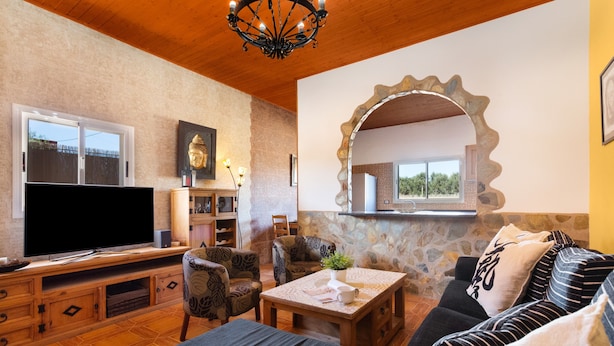 Una sala de estar con televisor, sofá, sillones, una mesa de centro y una pared de piedra con un espejo.