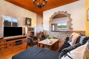 A living room with a TV, sofa, chairs, a coffee table, and a stone wall with a mirror. - Vacation Apartment 'Rural Zona Céntrica Isla' with Mountain View, Private Terrace and Wi-Fi (Puerto del Rosario)