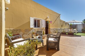 An outdoor patio with wicker furniture, a stone wall, and a door with a window. - Vacation Apartment 'Rural Zona Céntrica Isla' with Mountain View, Private Terrace and Wi-Fi (Puerto del Rosario)