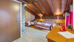 A wooden ceiling with exposed beams, a wooden door, two beds with plaid bedding, a wooden table with a red decoration, and a small Christmas tree.