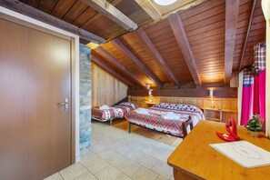 Un plafond en bois avec des poutres apparentes, une porte en bois, deux lits avec une literie à motifs écossais, une table en bois décorée de rouge et un petit sapin de Noël.