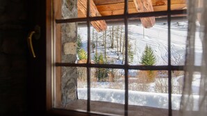 Una ventana con marco de madera y barrotes de metal, que muestra un paisaje nevado con árboles y un edificio a lo lejos.
