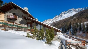 Un edificio de piedra con un balcón de madera, un telón de fondo montañoso y un paisaje cubierto de nieve.