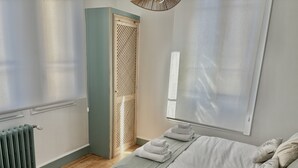 Une chambre à coucher comprenant un lit, une chaise, un radiateur, une porte en bois et une fenêtre avec des stores.