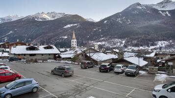 Un estacionamiento con varios autos, una iglesia con una aguja alta y montañas nevadas al fondo.