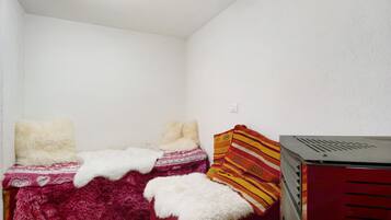 Een kleine kamer met een enkel bed, een rood-wit gebedde deken, zachte witte kussens en een rode verwarming.