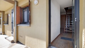 A building with a wooden door, a window with a wooden shutter, and a staircase leading to an upper floor. -  Le Carlit – Apartment in Les Angles with mountain view, cosy and functional (Les Angles)