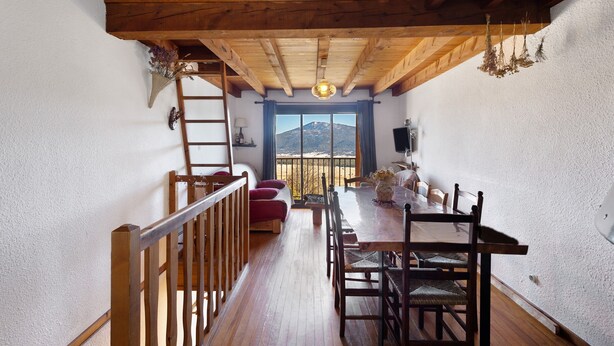 A dining area with a wooden table and chairs, a view of a mountain through a window, and a wooden ceiling. -  Le Carlit – Apartment in Les Angles with mountain view, cosy and functional (Les Angles)