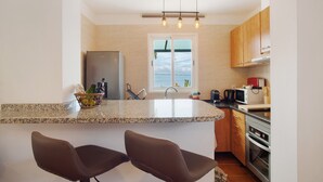 A kitchen with a granite countertop, stainless steel appliances, wooden cabinets, and a window with a view.